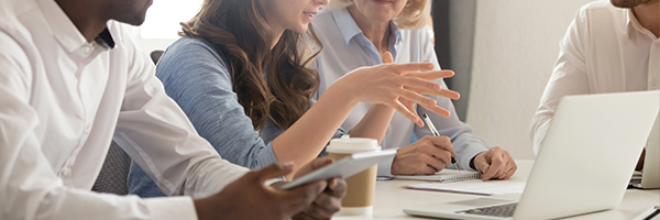 Groupe d'hommes et de femmes assis autour d'une table et regardant un ordinateur portable tout en discutant d'un projet.